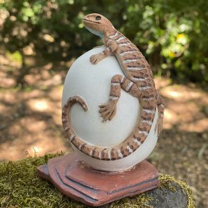 Laura Ames' hand sculpted brown ceramic lizard perched on white egg