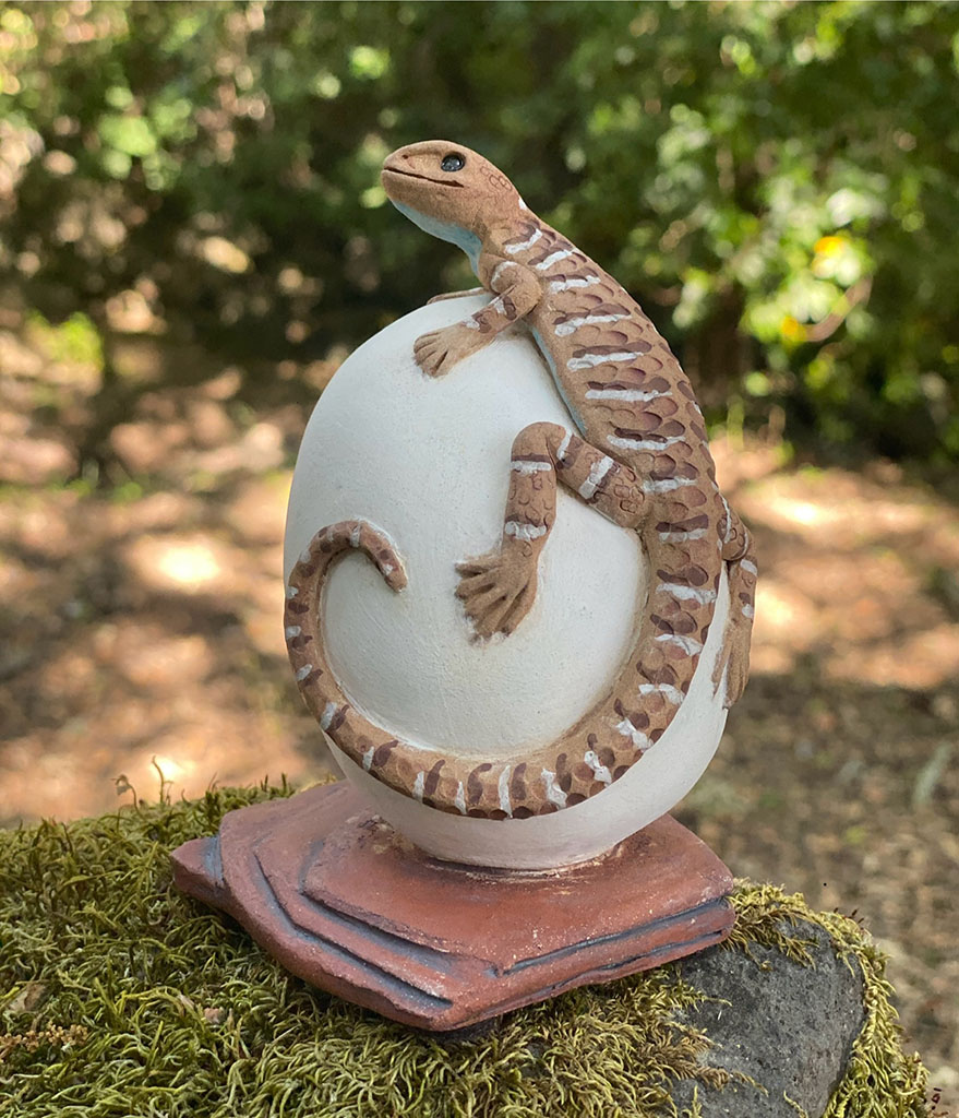 Laura Ames' hand sculpted brown ceramic lizard perched on white egg