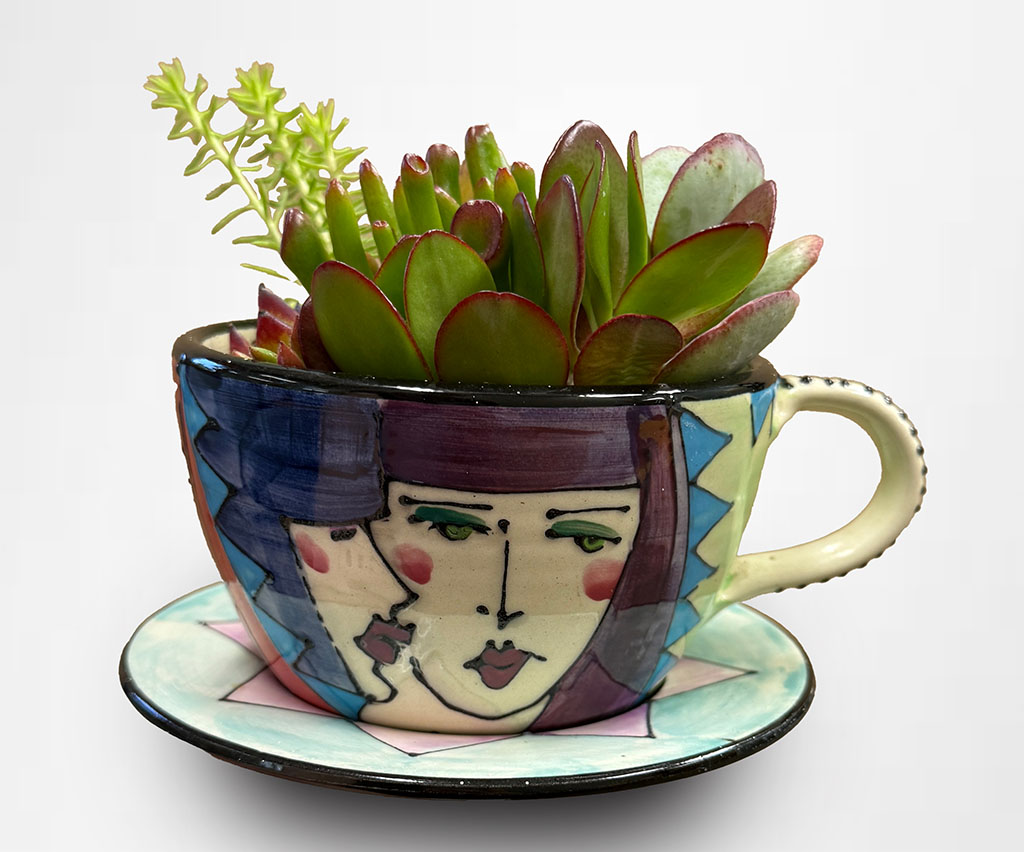 Denise Ford hand painted cup and saucer with succulents. Cup has a male and female face on the front