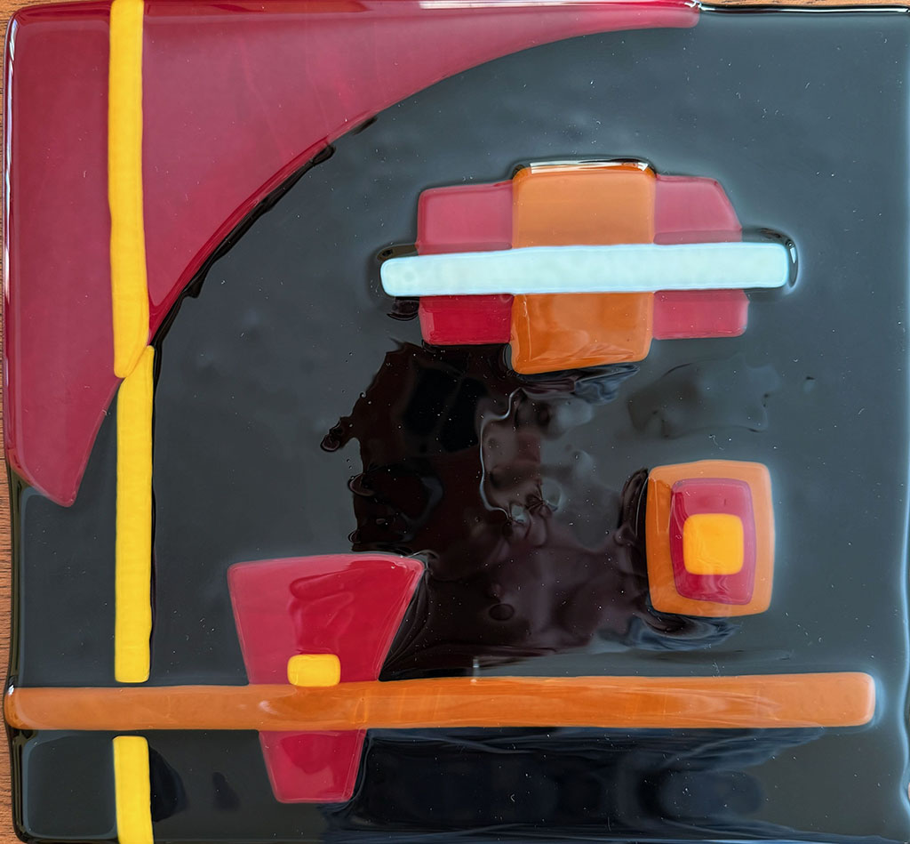 Frances Fuch's fused glass abstract art piece with geometric pieces in white, orange and black on red background